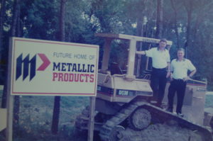 men with a bulldozer and sign indicating the future home of Metallic Products, illustrating an article about Metallic Products history